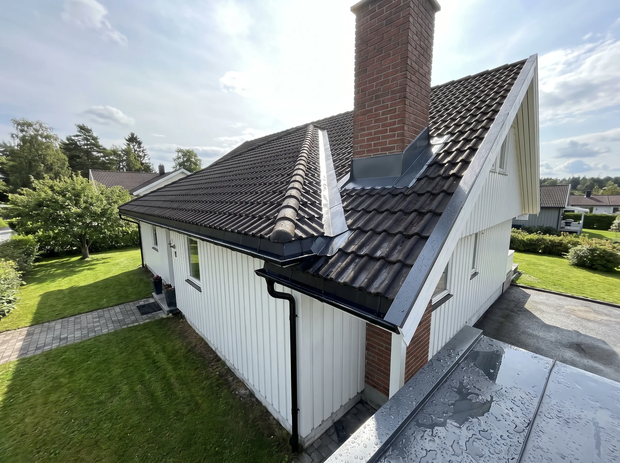Taket på et hus med mursteinspipe og hvit fasade i et frodig grønt område