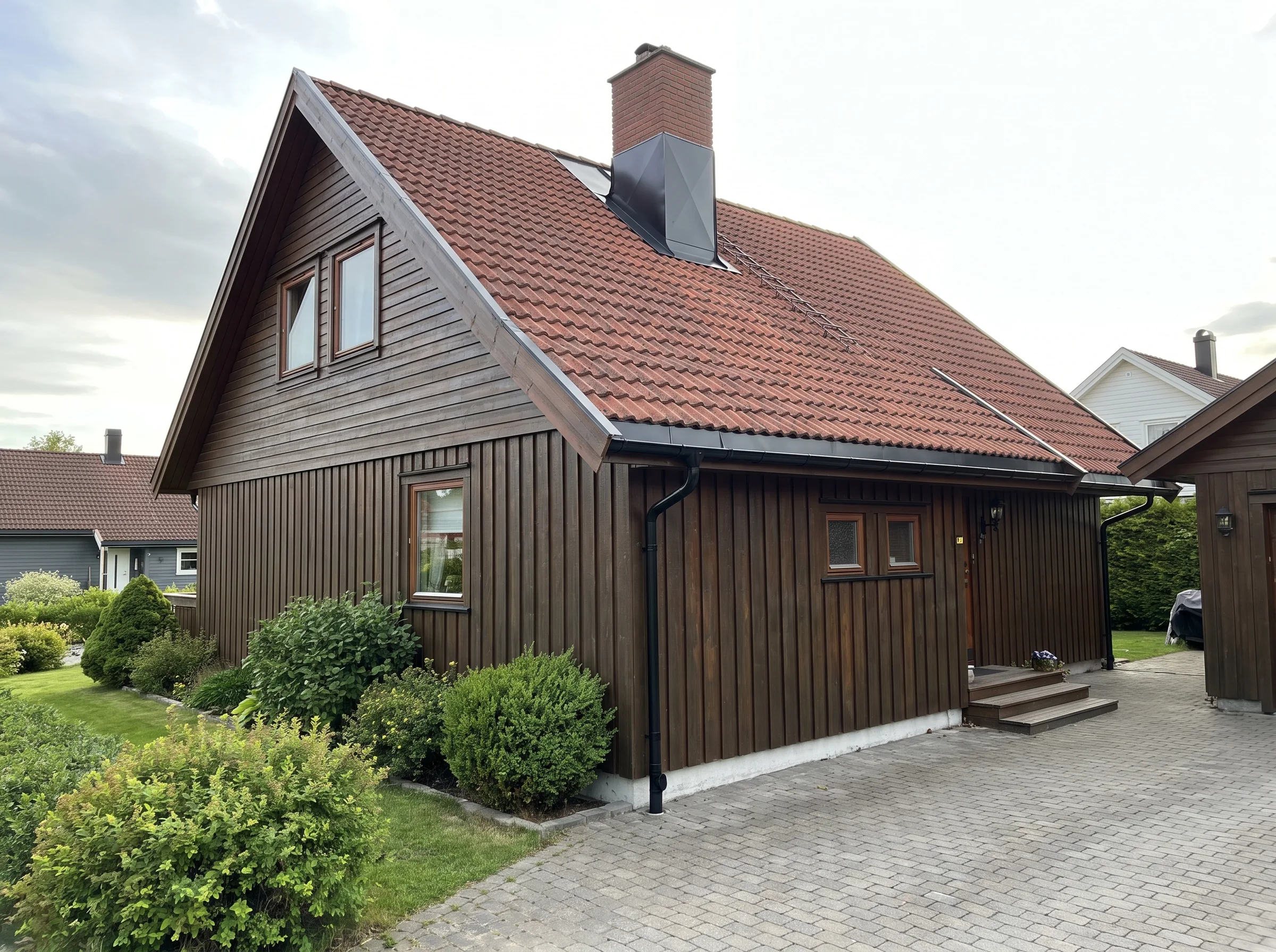 En velholdt enebolig med trepanel og rød takstein, omkranset av grønt landskap