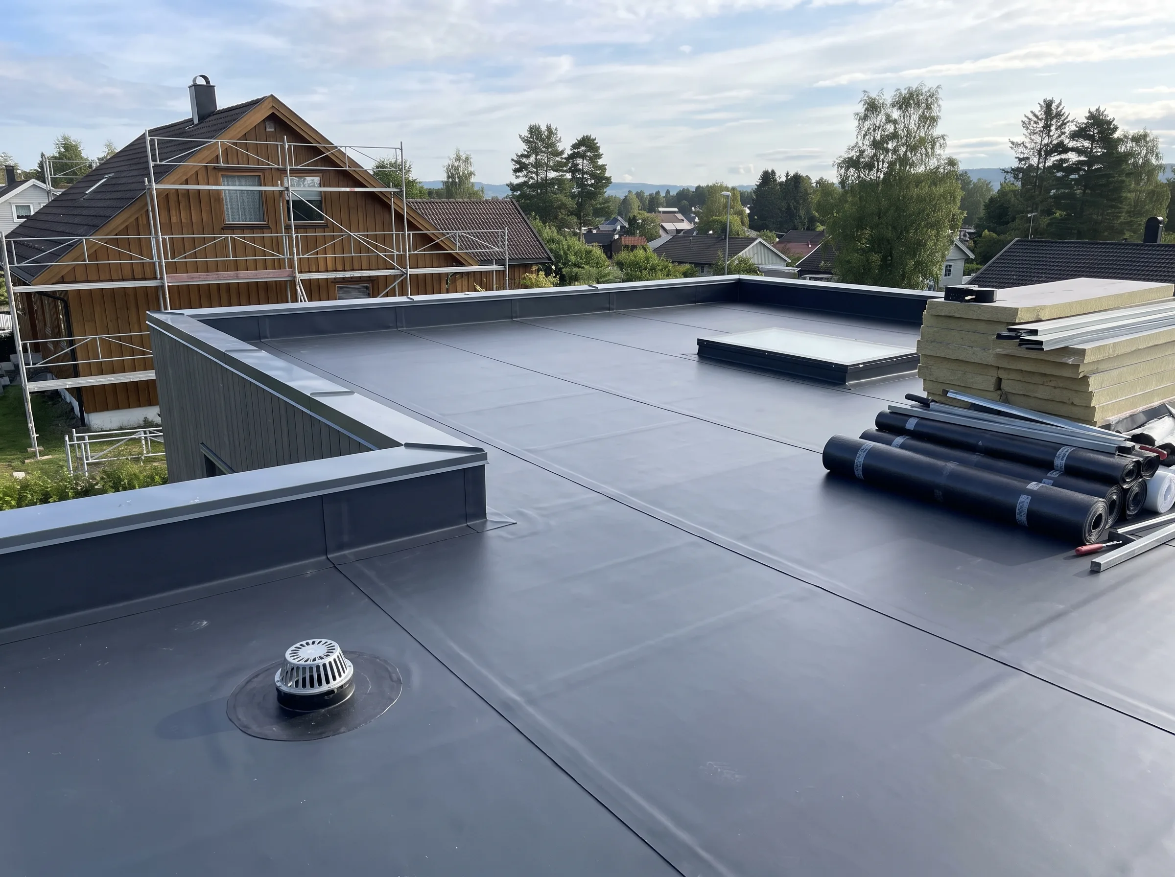 Flat tak med materialer for taktekking i bakgrunn av hus