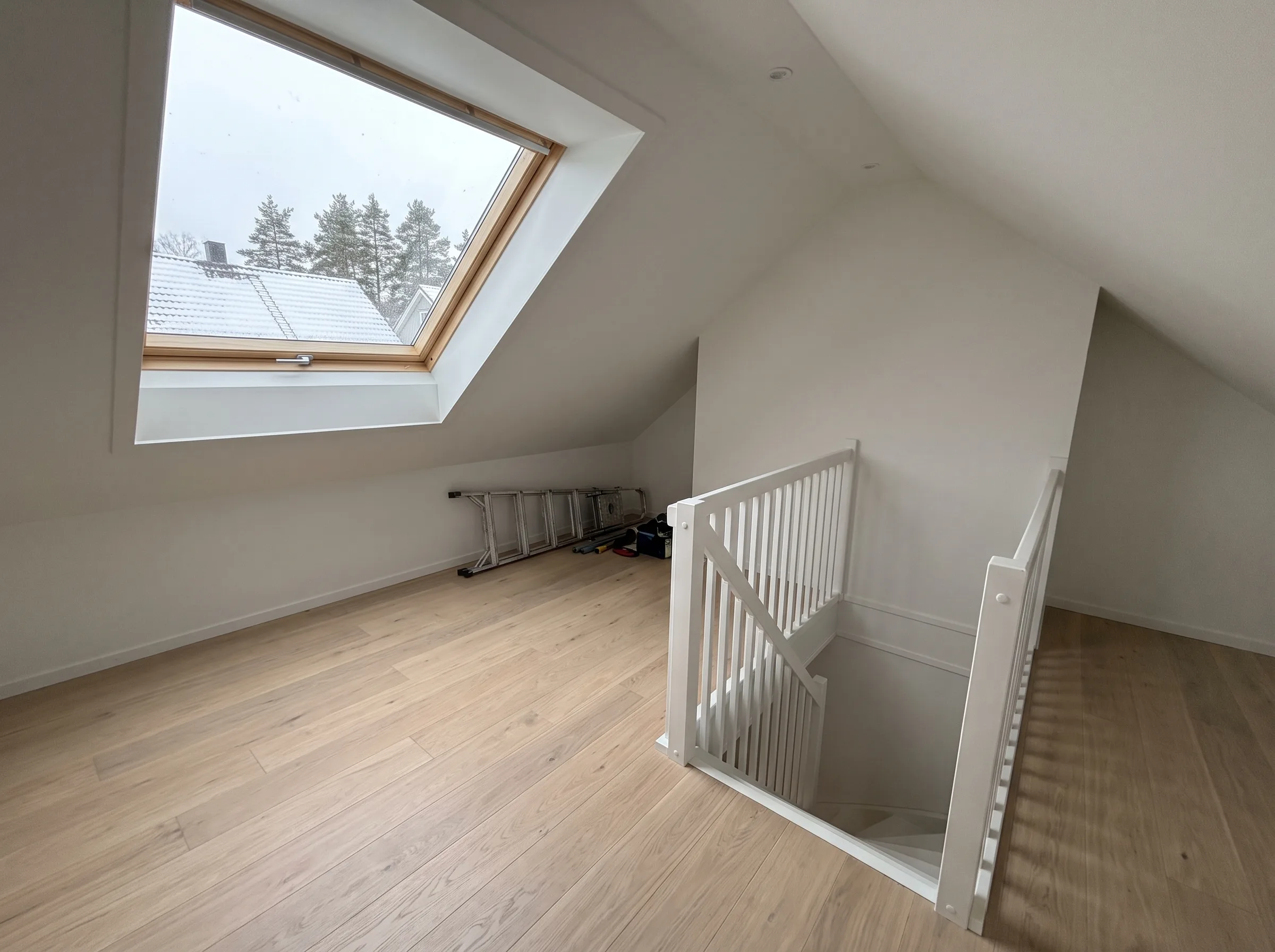Lys og moderne loftstue med vindu og trapp i hvitt interiør