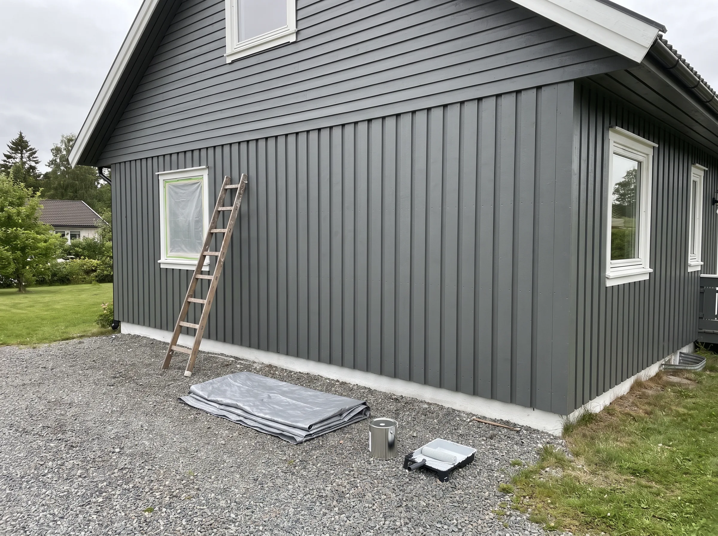 Maling av fasade på et hus med stige og malerutstyr