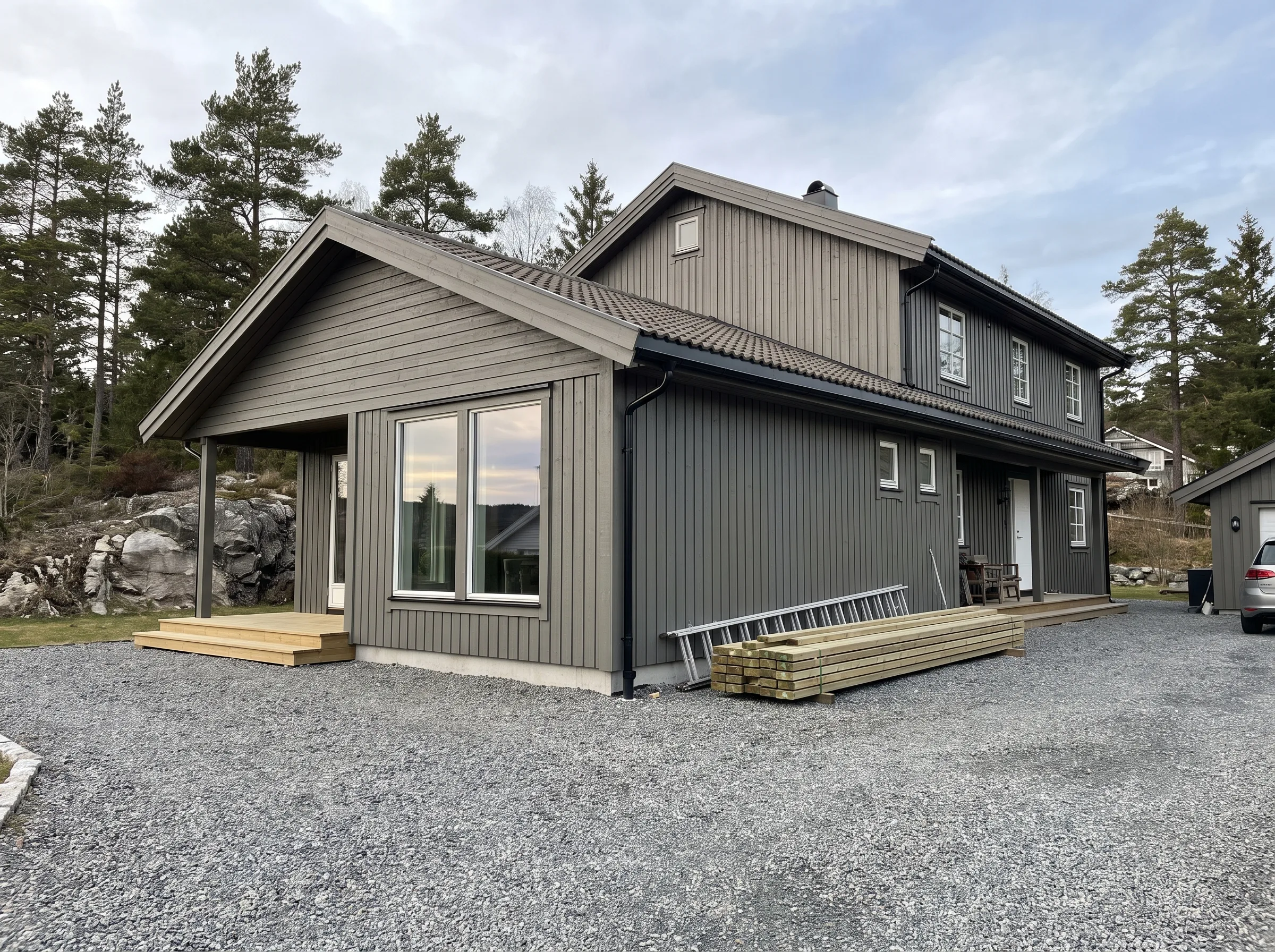Fasadearbeid på et moderne hus med tilbygg og steinlagt gårdsplass